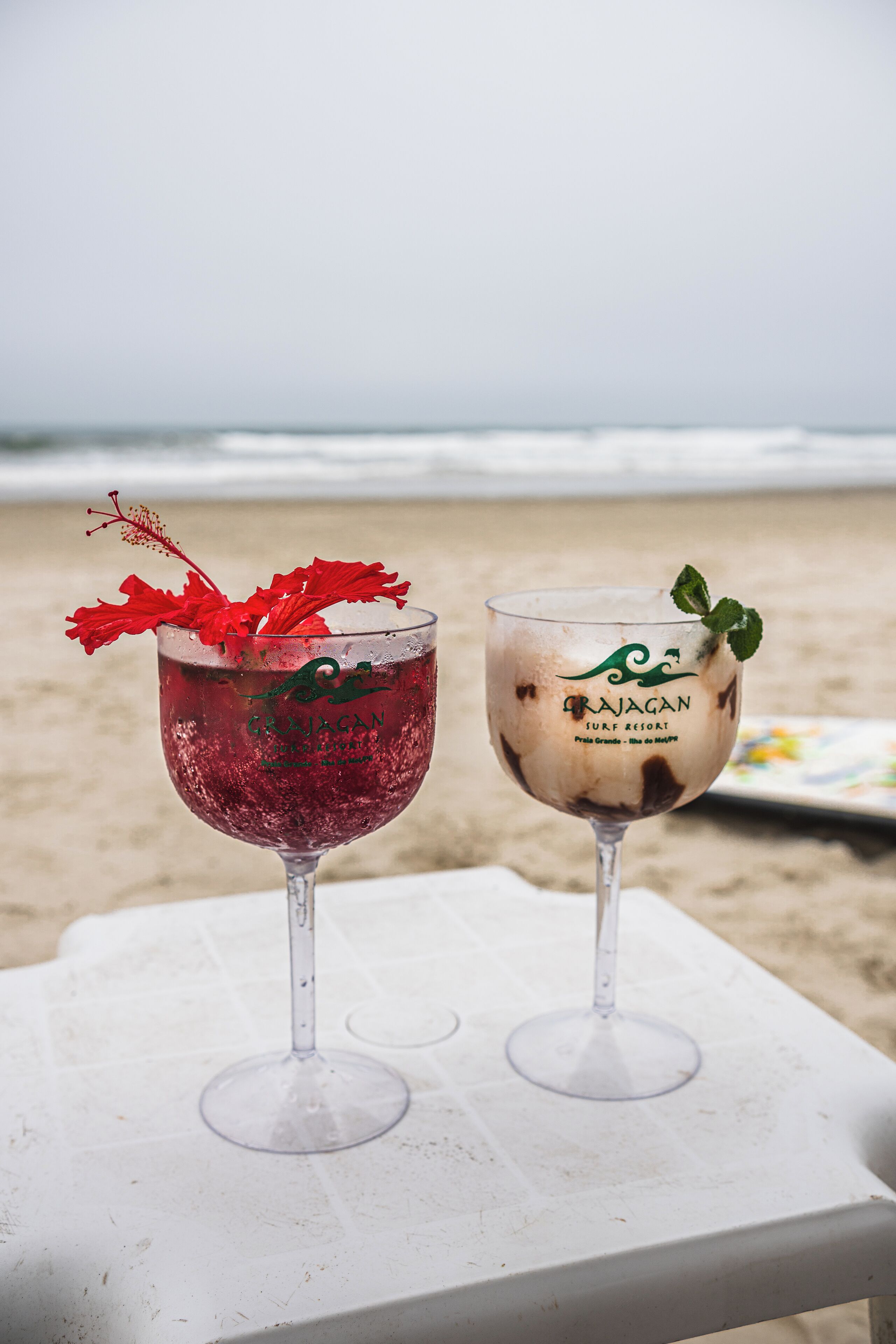 Two glasses of beverages on a white table by the beach.