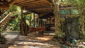 A covered wooden structure with a stone pathway, wooden benches, and a waterfall. - Grajagan Surf Resort (Paranaguá)