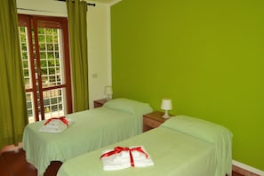 Habitació amb dos llits, parets verdes, una finestra amb cortines i vistes a vegetació.