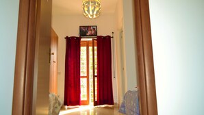 Un couloir avec une porte en bois, des rideaux rouges et un luminaire au plafond.