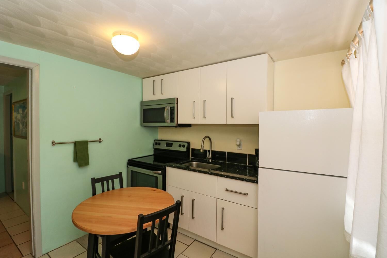 A compact kitchen with a wooden dining table, white cabinets, a microwave, stove, sink, and a refrigerator.