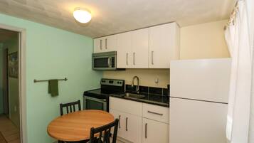 A compact kitchen with a wooden dining table, white cabinets, a microwave, stove, sink, and a refrigerator.
