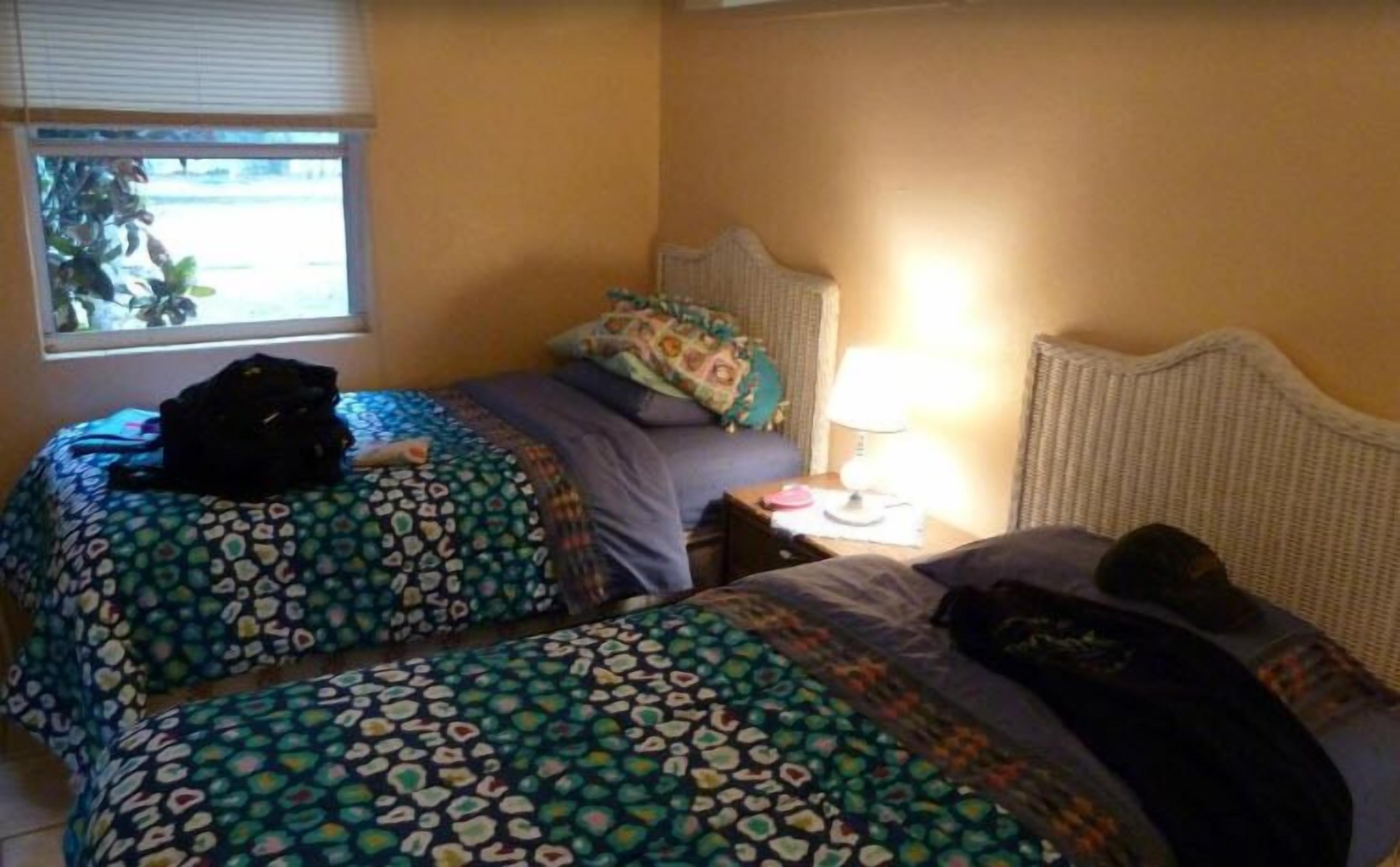 Een hotelkamer met twee bedden, een raam, een lamp en een koffer op de vloer.