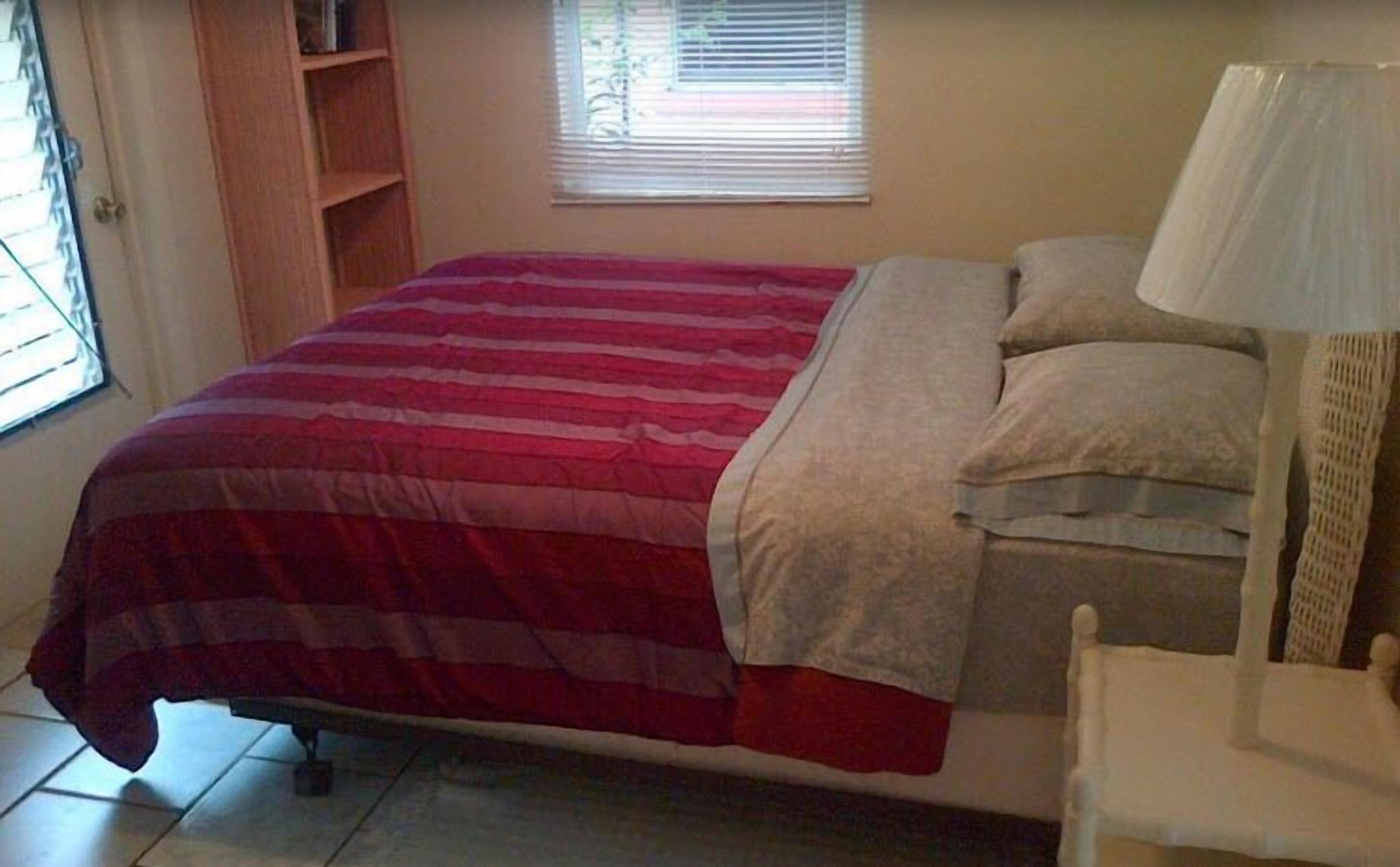 A single bed with a red and white striped bedspread, a white pillow, and a white bedside table with a lamp.