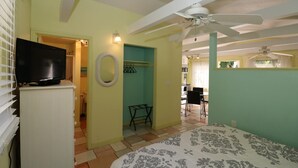 Una habitación con una cama, un ventilador de techo, un televisor sobre un mueble y un baño visible a través de una puerta abierta.