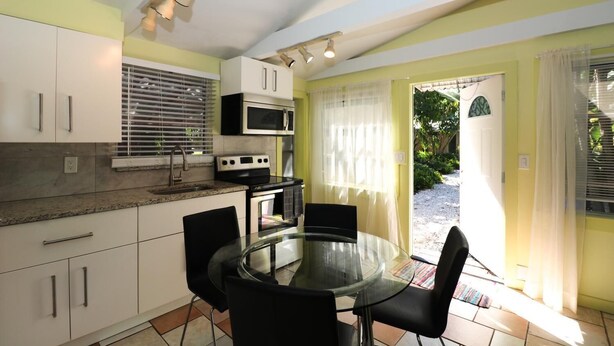 Una cocina compacta con armarios blancos, microondas, estufa y una mesa de vidrio con sillas.