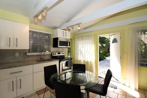 Una cocina compacta con armarios blancos, microondas, estufa y una mesa de vidrio con sillas.