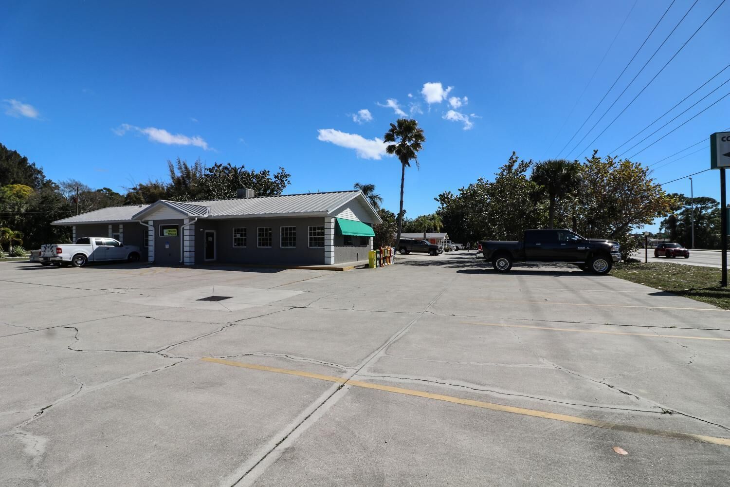A building with a green awning, a parking lot, and a palm tree.