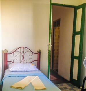 A single bed with a metal headboard, a green door, and a fan in the corner. - Hostel da Providencia (Salvador)