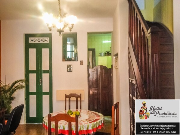 A dining area with a round table, chairs, a chandelier, and a green door. - Hostel da Providencia (Salvador)