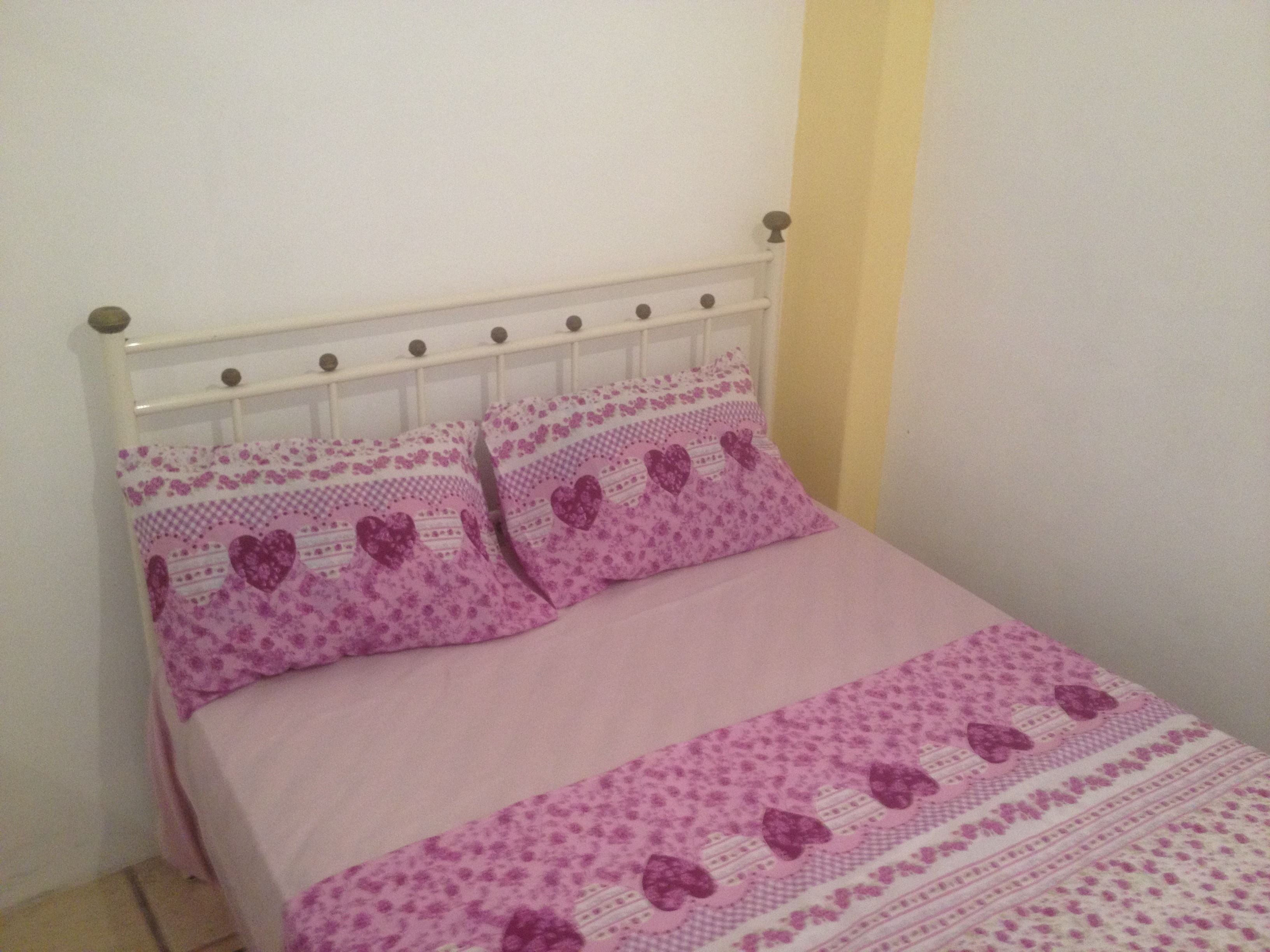 Ein Bett mit weißem Metallgestell und einer rosa Bettdecke mit Blumenmuster.