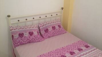 Ein Bett mit weißem Metallgestell und einer rosa Bettdecke mit Blumenmuster.