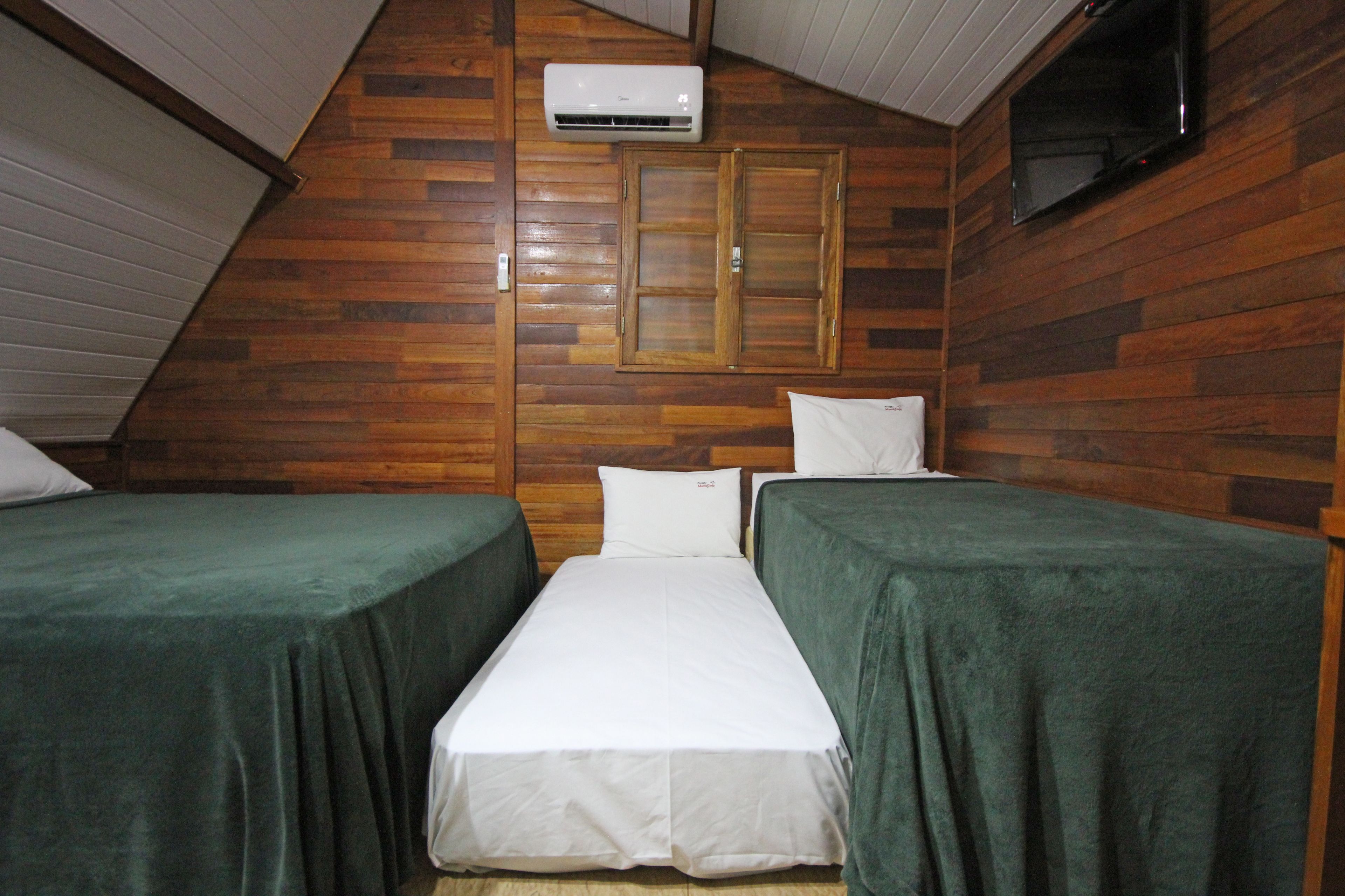 A room with wooden walls, a flat-screen TV mounted on the wall, and two beds with green bedspreads.
