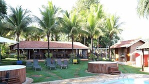 A poolside area with lounge chairs, a hot tub, and a building with a tiled roof. - Pousada Monte Carlo (Olímpia)