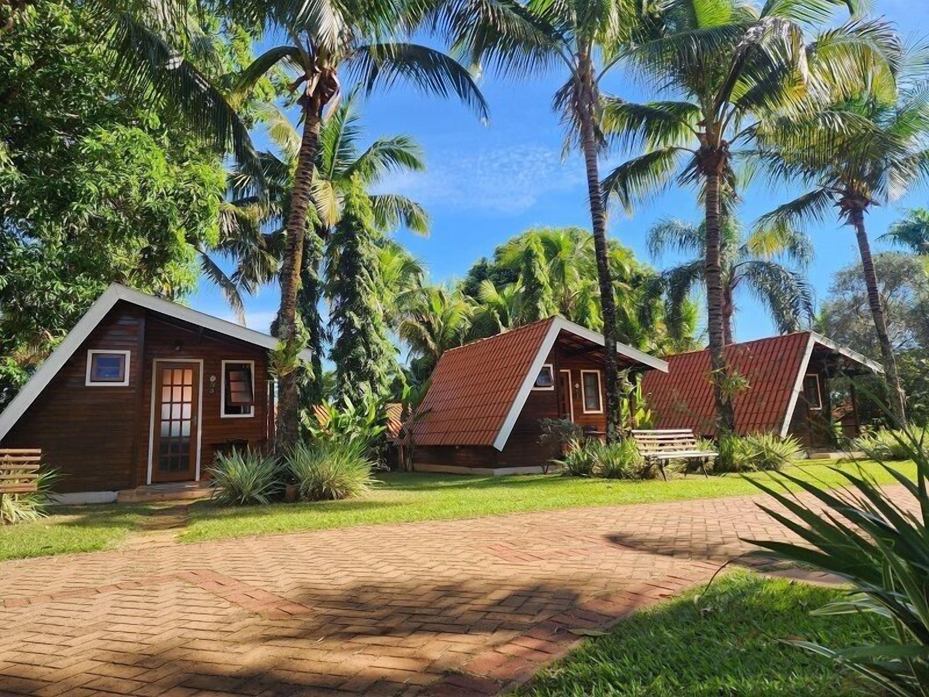 A bungalow-style accommodation with a brick pathway leading to the entrance, surrounded by lush greenery and palm trees.