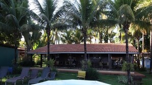 A hot tub in a garden with palm trees and a building with a tiled roof. - Pousada Monte Carlo (Olímpia)