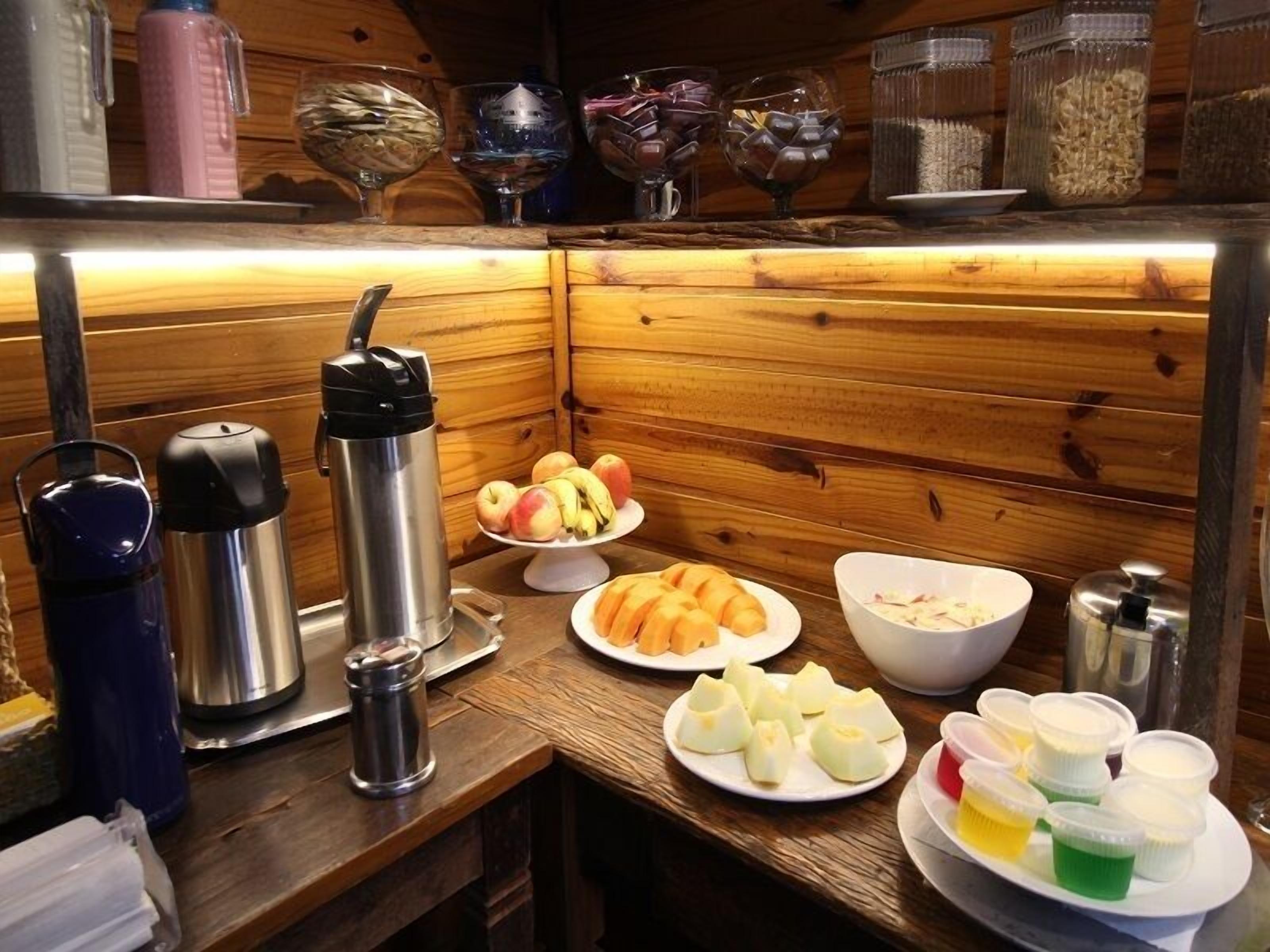 Ein Interieur einer Holzhütte mit einem Frühstücksbuffet, darunter Früchte, Gebäck und Getränke.