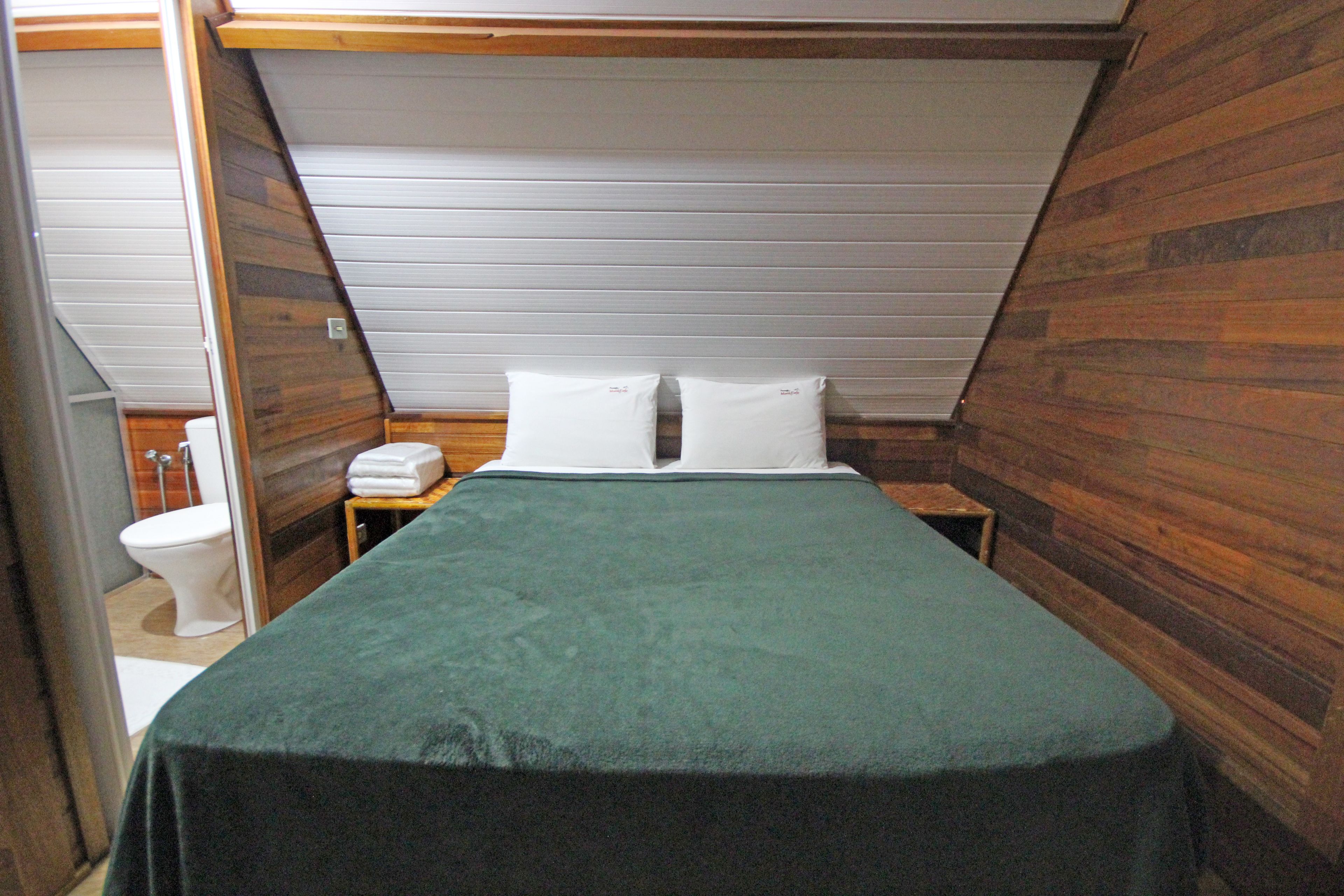 Una habitación pequeña con paneles de madera, una cama individual, una mesita de noche y un inodoro.