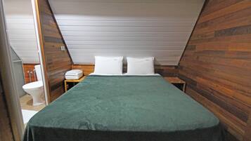 Una habitación pequeña con paneles de madera, una cama individual, una mesita de noche y un inodoro.
