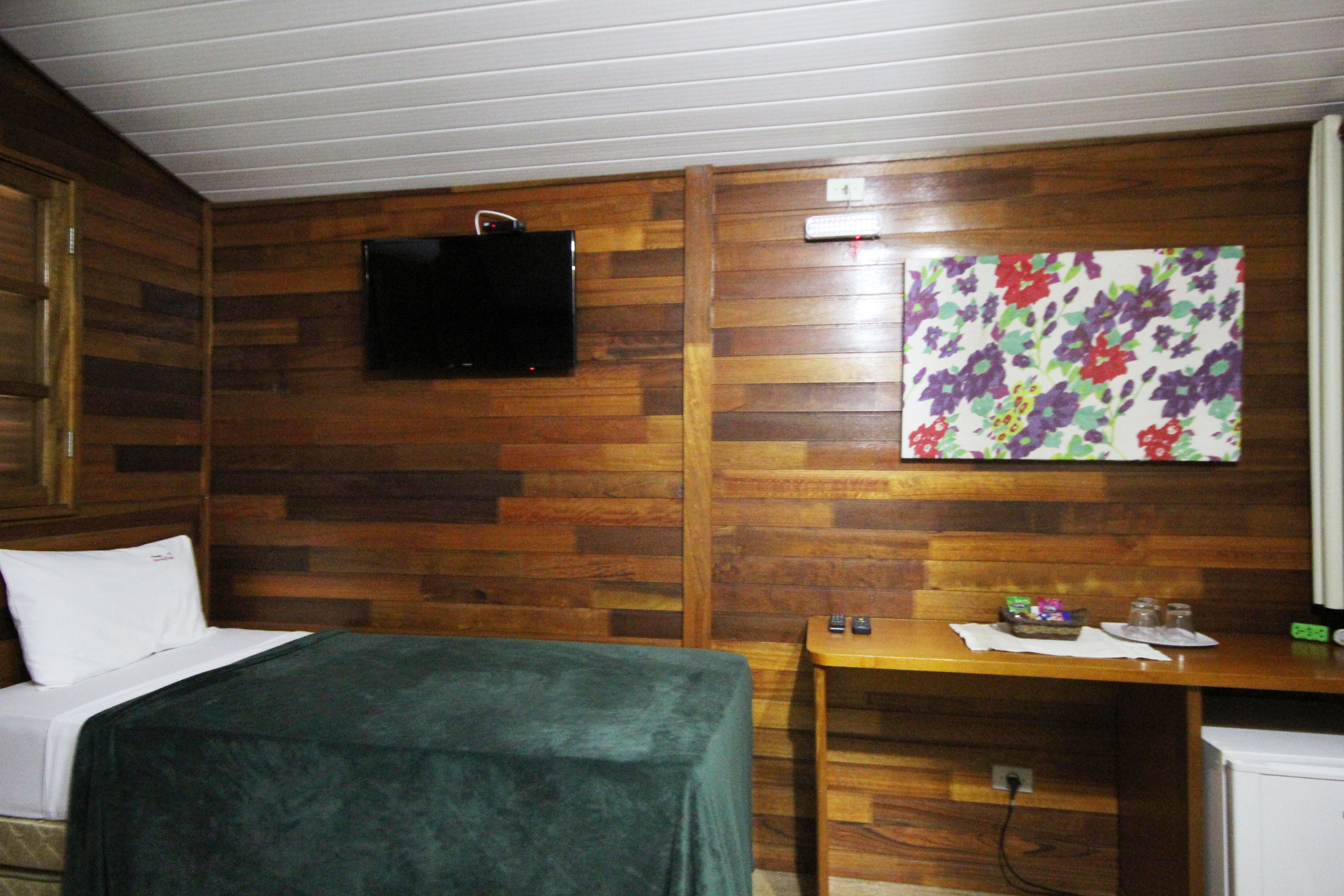 Habitació d'hotel amb llit, escriptori, televisió penjada a la paret i una obra d'art floral sobre l'escriptori.