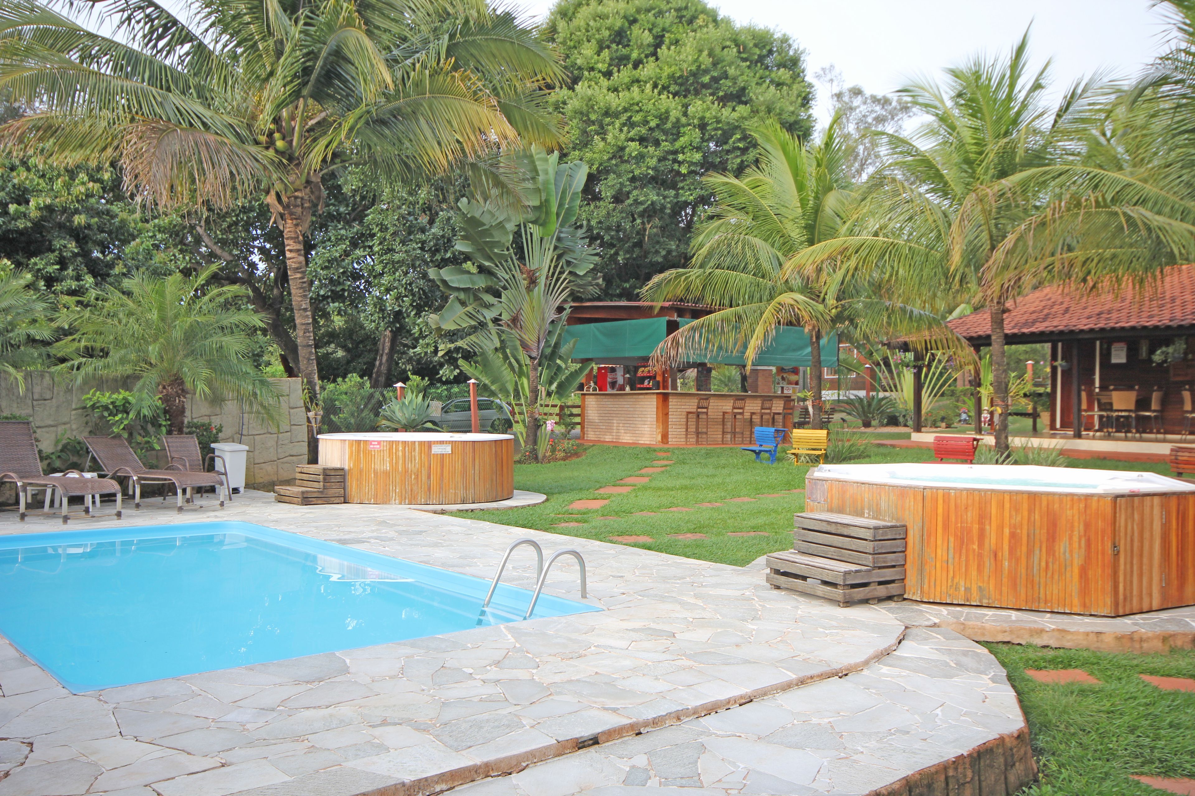 Una piscina con baldosas de piedra, jacuzzis de madera y un área verde con palmeras.
