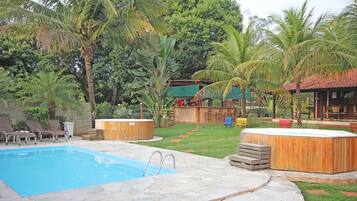 Una piscina con baldosas de piedra, jacuzzis de madera y un área verde con palmeras.