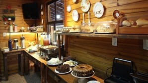 A cozy cabin-style kitchen with wooden walls, a long counter with various food items, and a wall-mounted TV. - Pousada Monte Carlo (Olímpia)