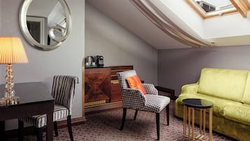 A room with a dining table, two chairs, a sofa, a small side table, a lamp, a coffee maker, and a mirror.