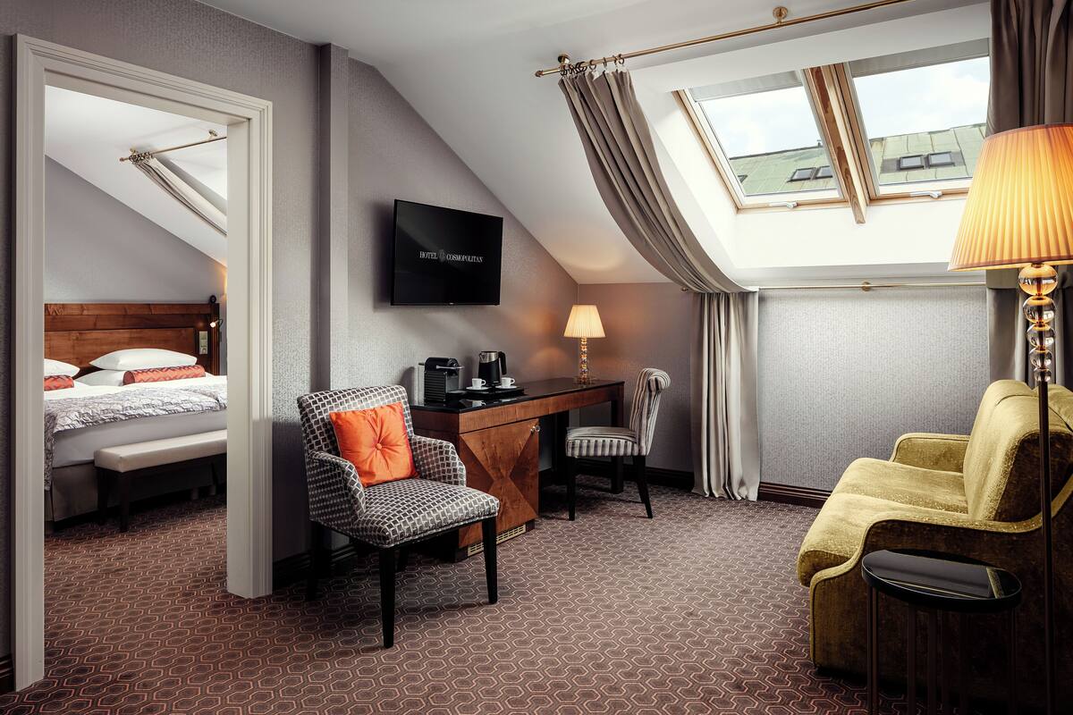 A hotel room with a bed, a desk, two chairs, a TV, and a window with curtains.