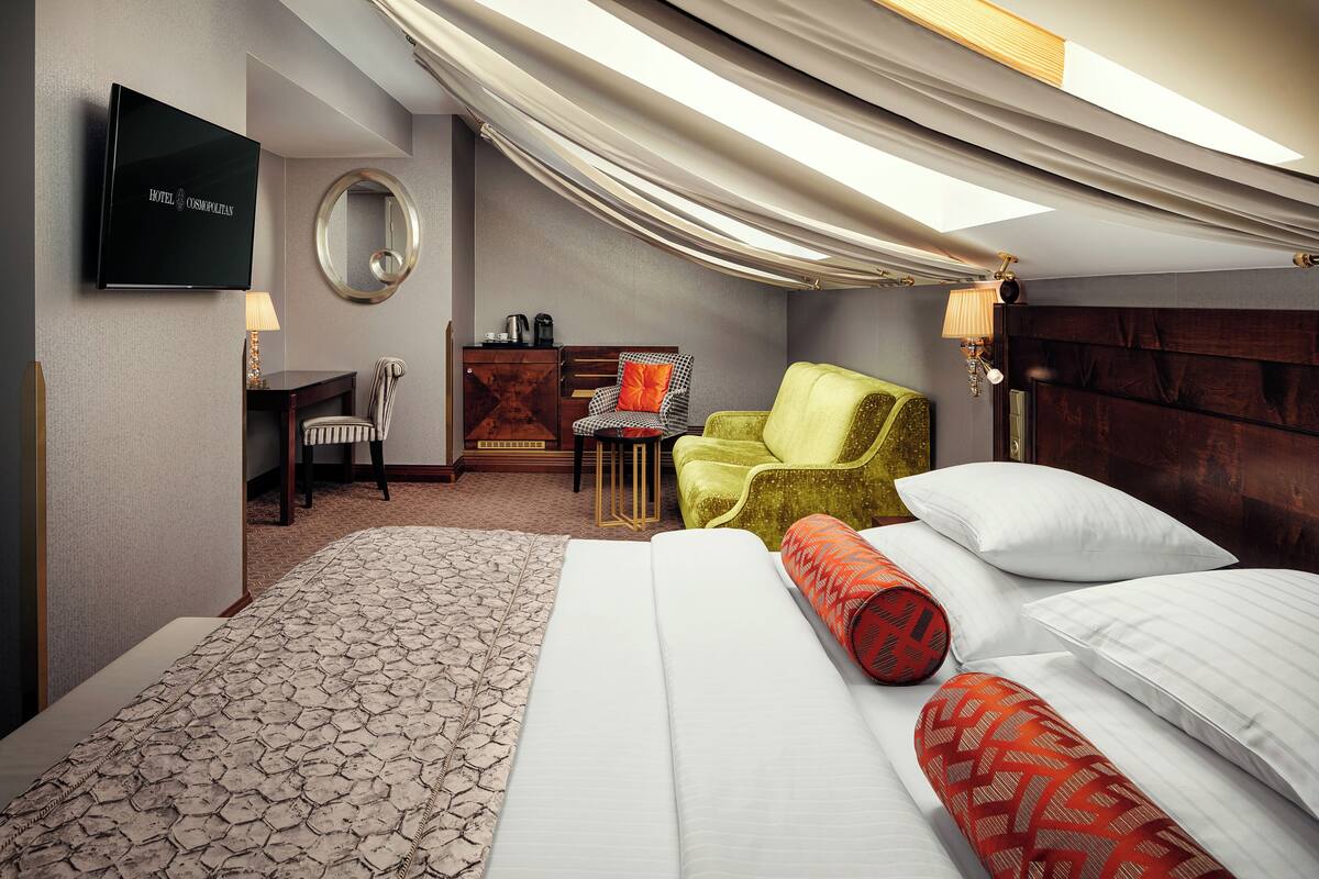 A hotel room with a bed, a desk, a chair, a TV, and a mirror.