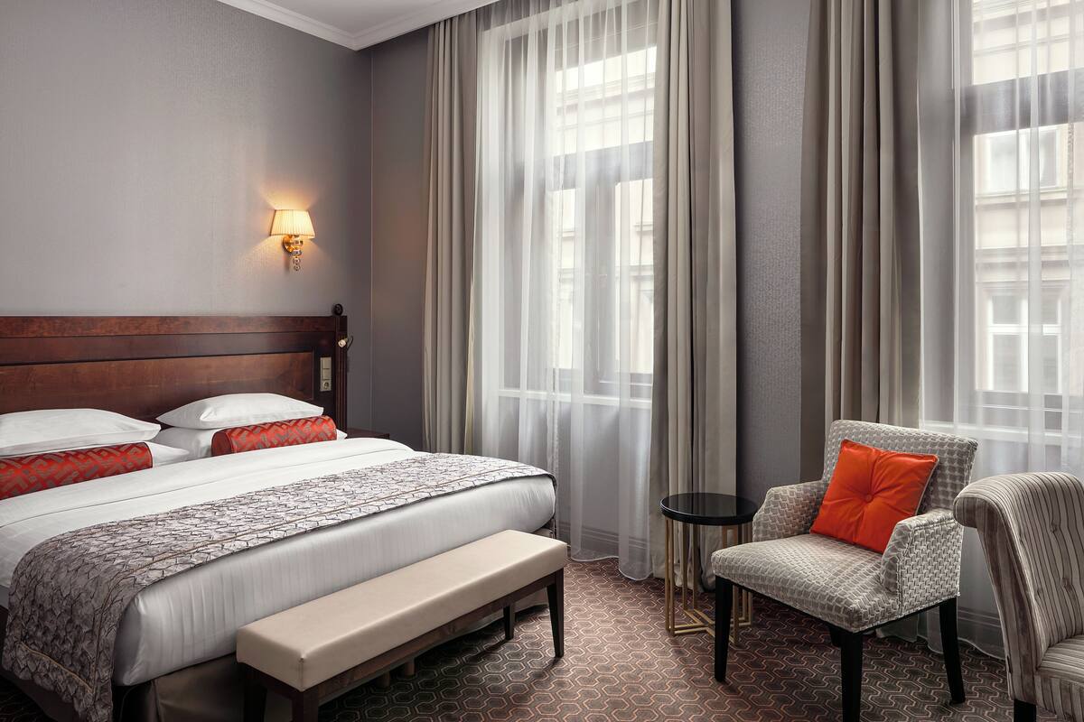 A hotel room with a large bed, a bench, a chair, and a small table.