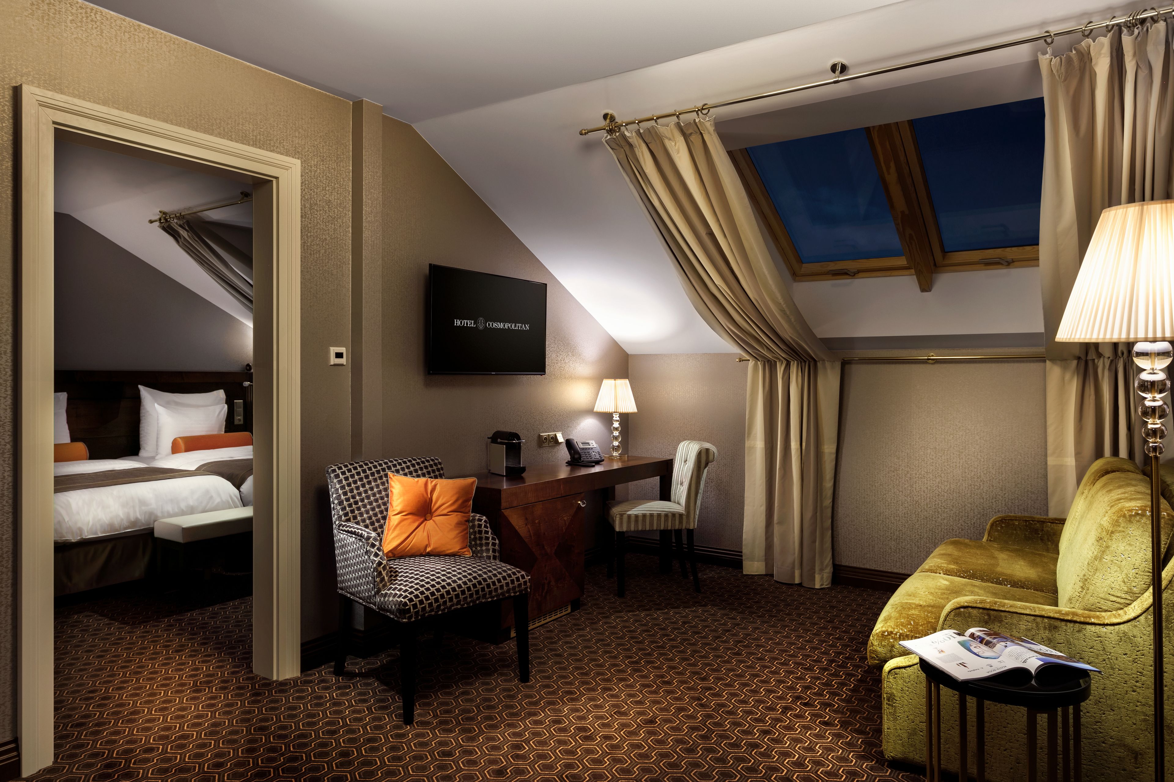 A hotel room with a bed, a desk with a lamp, a chair, and a sofa.