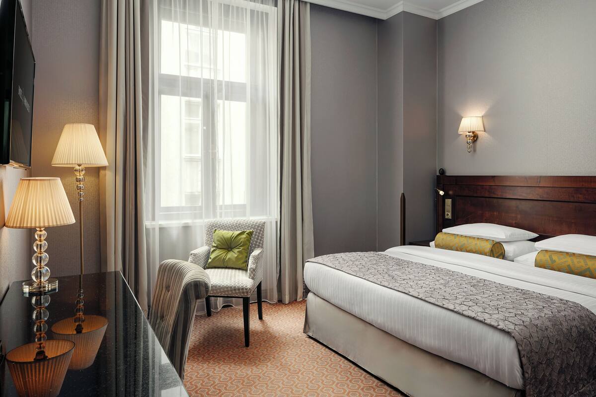 A hotel room with a bed, a chair, a desk, and a lamp.
