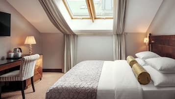 Una habitación de hotel con cama, escritorio, silla, lámpara y ventana con cortinas.