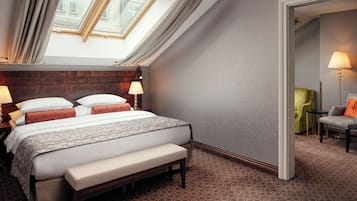 Habitación de hotel con una cama grande, un banco, un tragaluz, una lámpara y una silla.