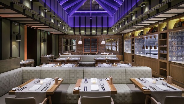 En restaurant med et moderne interiør, med et centralt siddeområde med polstrede bænke og borde dækket til spisning.