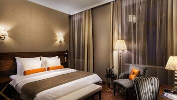 Una habitación de hotel con una cama grande, un banco, una silla y una mesita.
