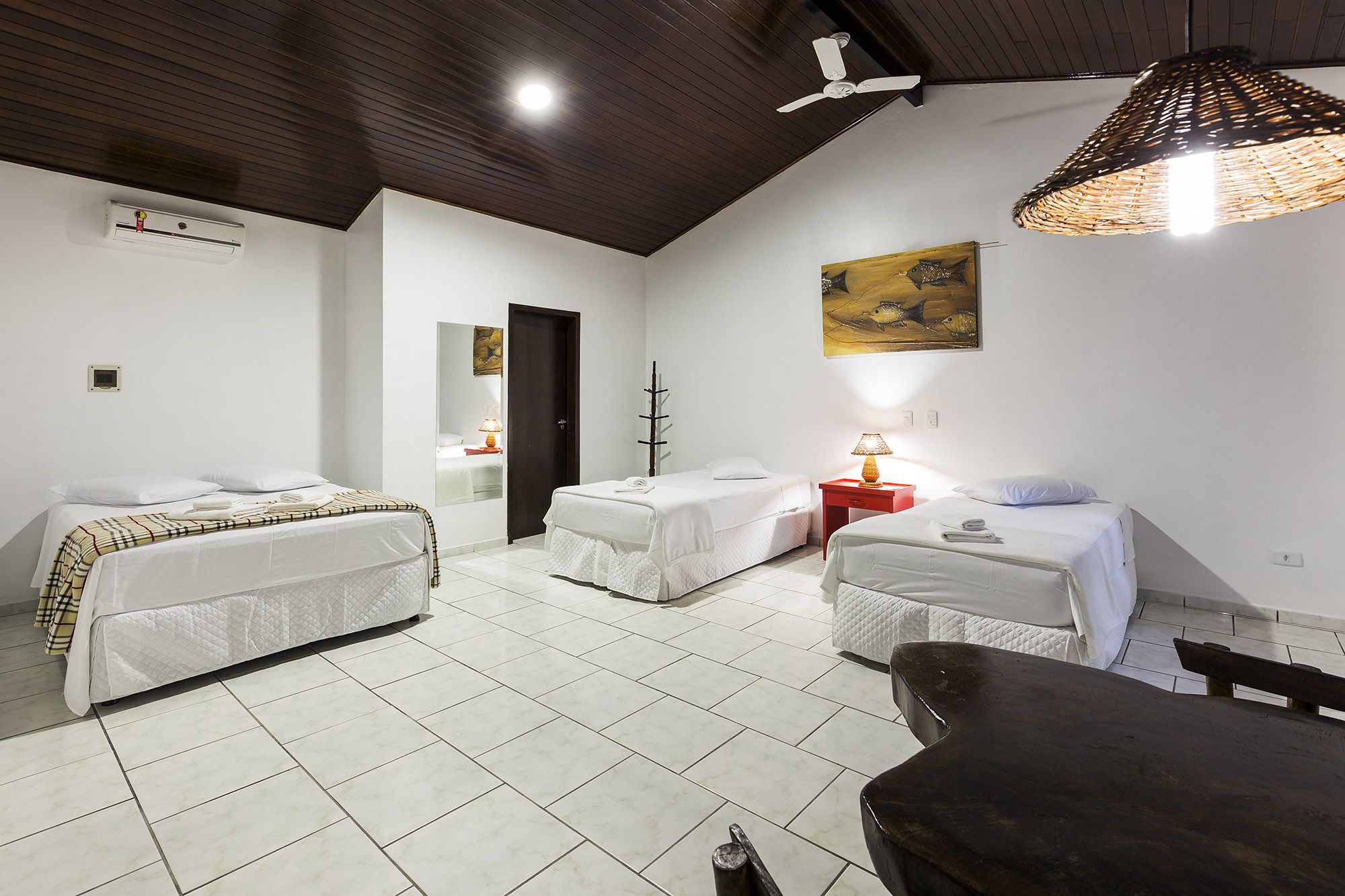 Quarto de hotel com duas camas, teto de madeira, luminária trançada grande e um quadro na parede.