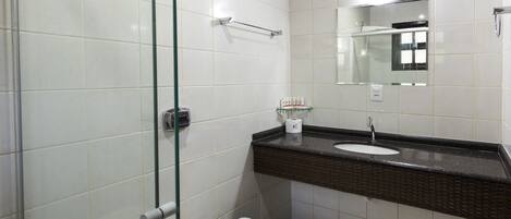 A modern bathroom with a glass shower enclosure, a white toilet, a dark brown sink with a mirror above, and a white tiled wall.