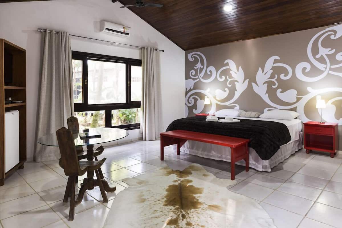 Een slaapkamer met een bed, een houten stoel, een glazen tafel, een bankje en een decoratieve wand.