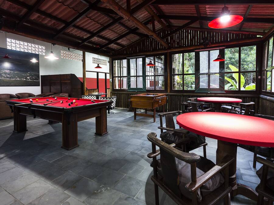 A pool table, foosball table, and billiard table in a room with large windows and red tables.