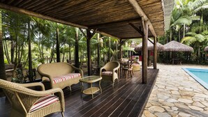 Un espace extérieur abrité, aménagé avec des meubles en osier, une piscine en pierre et une végétation tropicale.