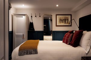 Una habitación de hotel con una cama, una puerta, perchero, un cuadro enmarco y un espejo.