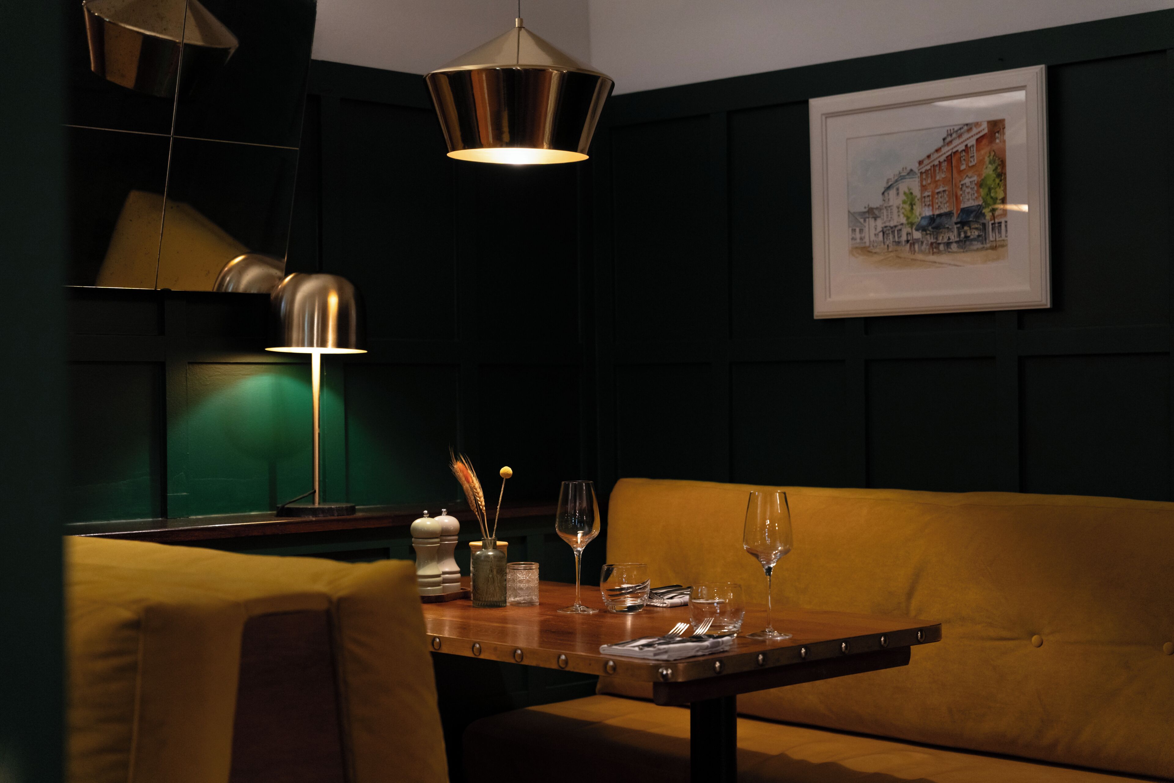 A dining area with a table set for two, a sofa, and a framed picture on the wall.