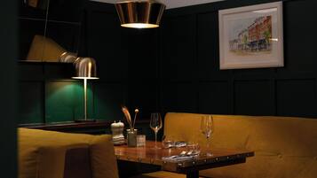A dining area with a table set for two, a sofa, and a framed picture on the wall.