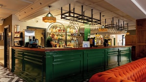 Una zona de bar con un camarero, una barra verde y un área de asientos con un sofá rojo.