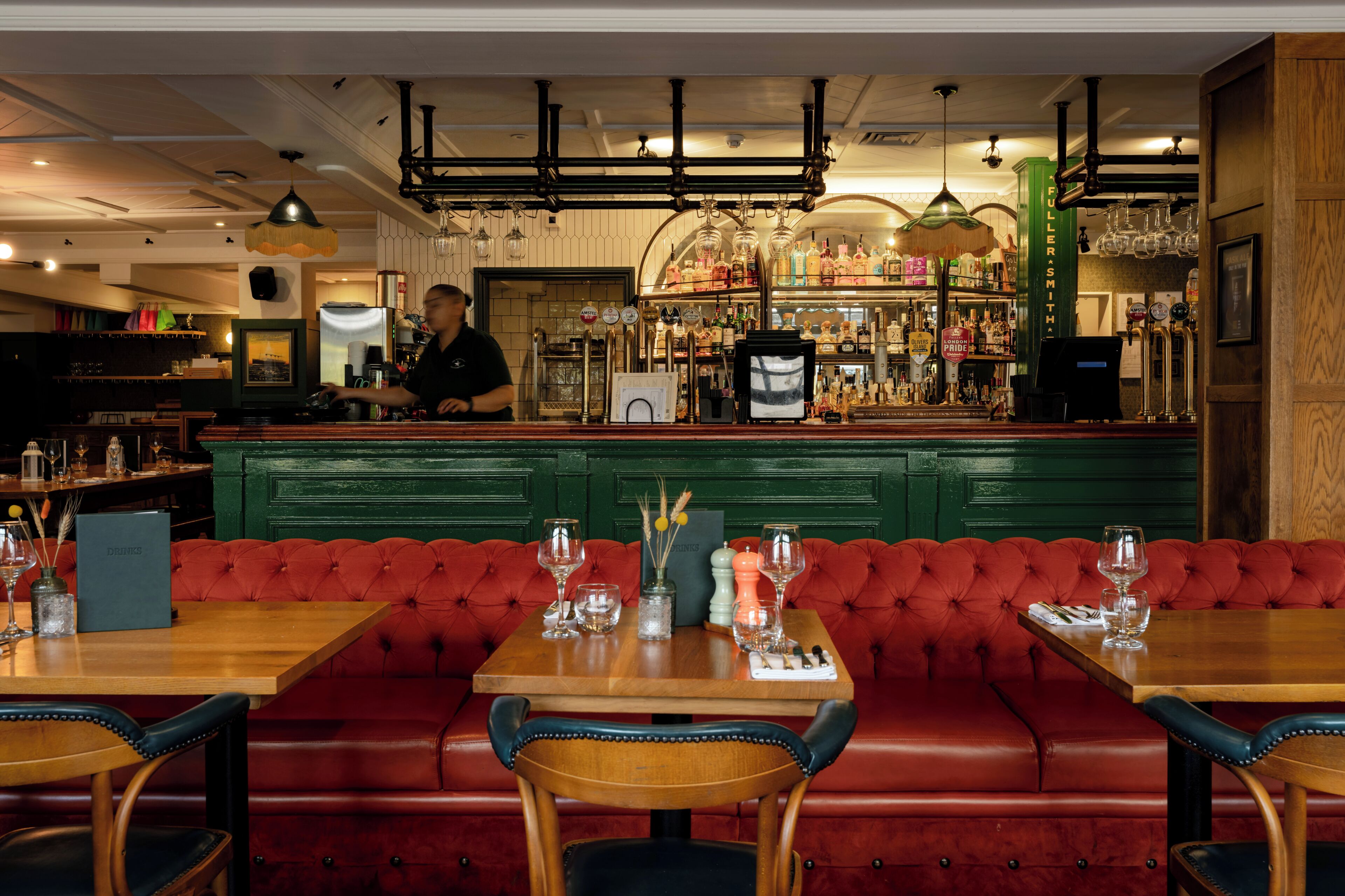 Un restaurante con una zona de bar, asientos tapizados en rojo y mesas de madera.