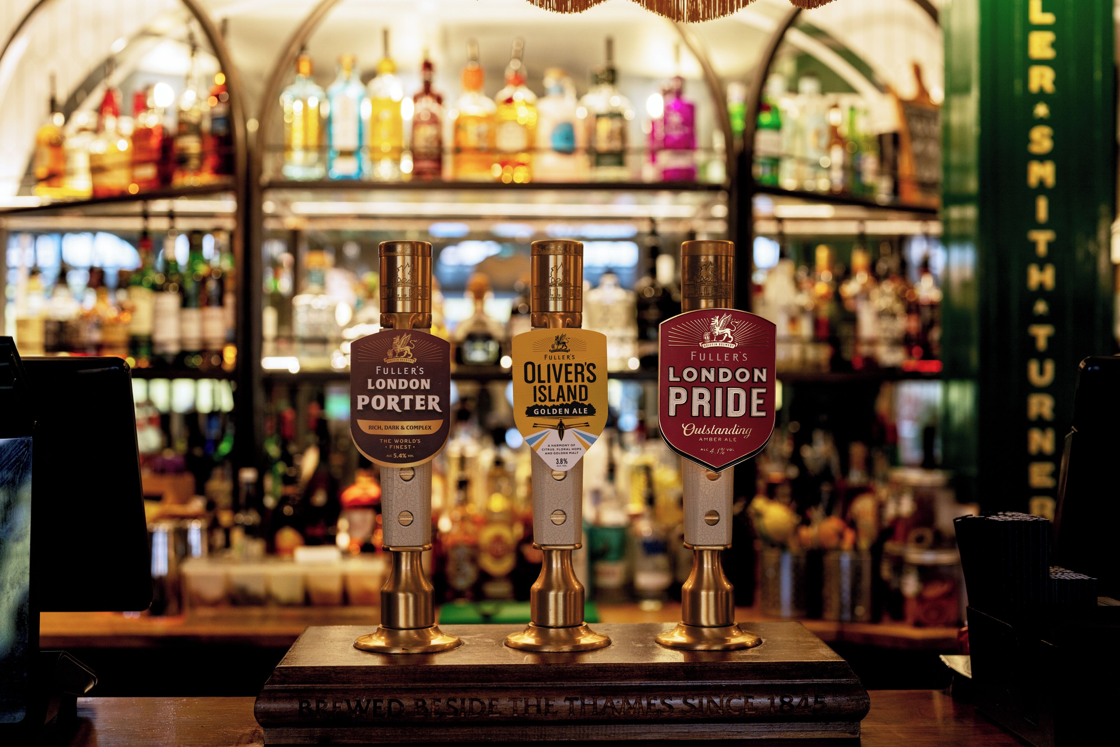 Eine Bar mit drei Hähnen, beschriftet mit 'London Porter', 'Oliver's Island Golden Ale' und 'London Pride'.
