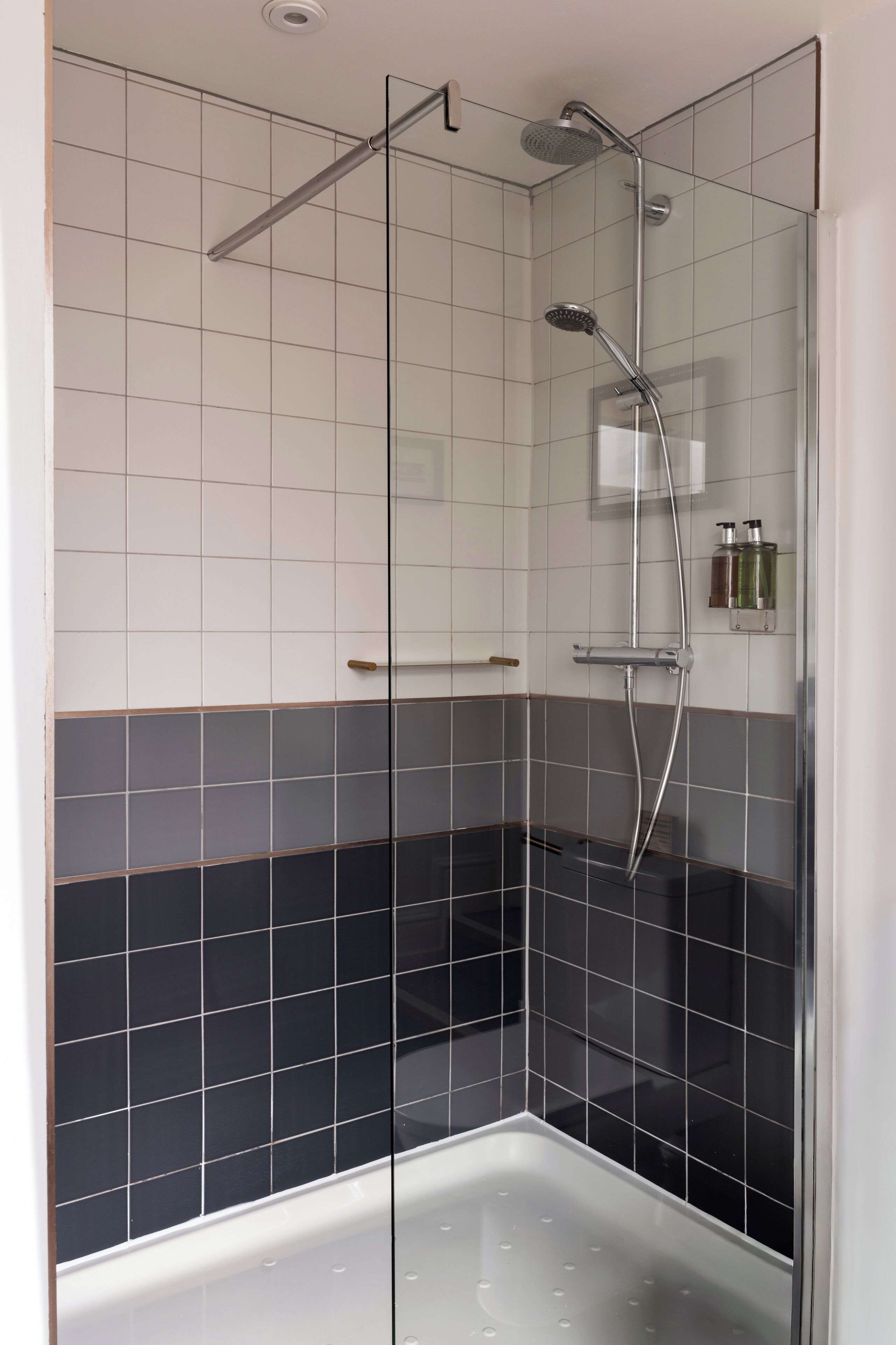 Une douche fermée par des parois en verre, dotée d’un pommeau de douche à main, d’un robinet mural et d’un panneau de commande.