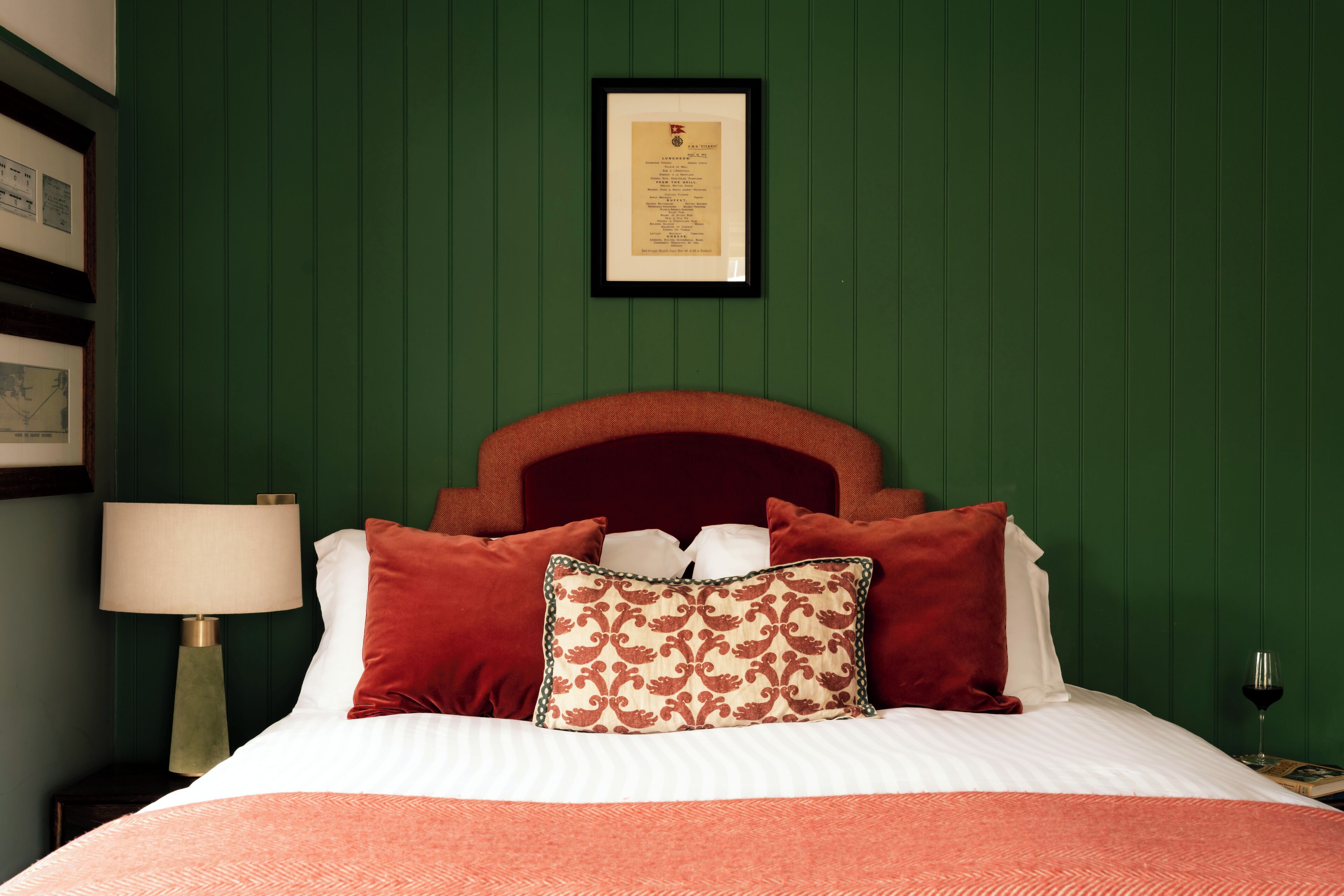 A neatly made bed with a red headboard, a framed certificate on the wall, and a bedside lamp.